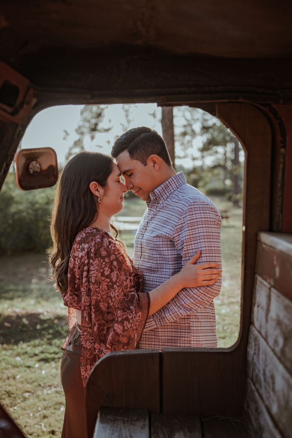 A couple embraces in a rustic wooden barn setting during a romantic photoshoot at sunset.