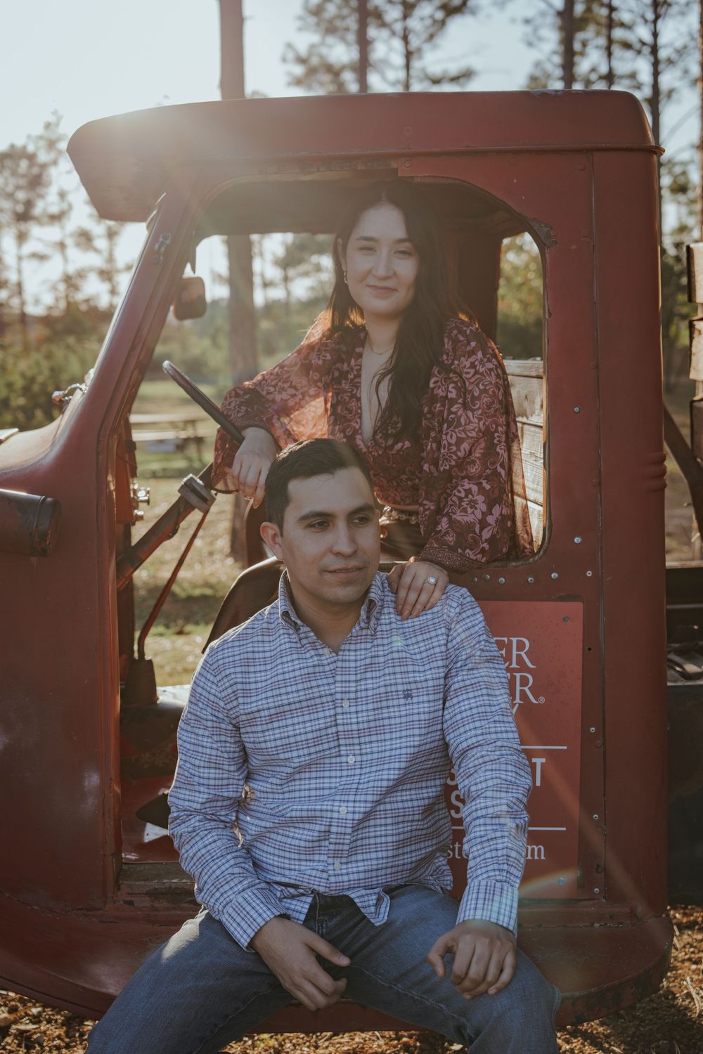 Two people pose together in front of a vintage red truck during a countryside photoshoot.