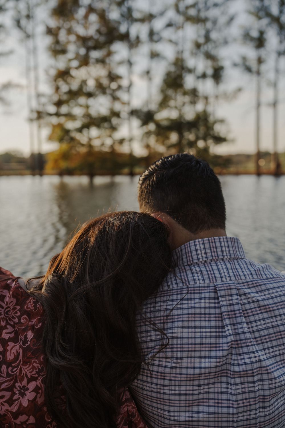 Silhouetted couple in close embrace against a pine forest backdrop at dusk.