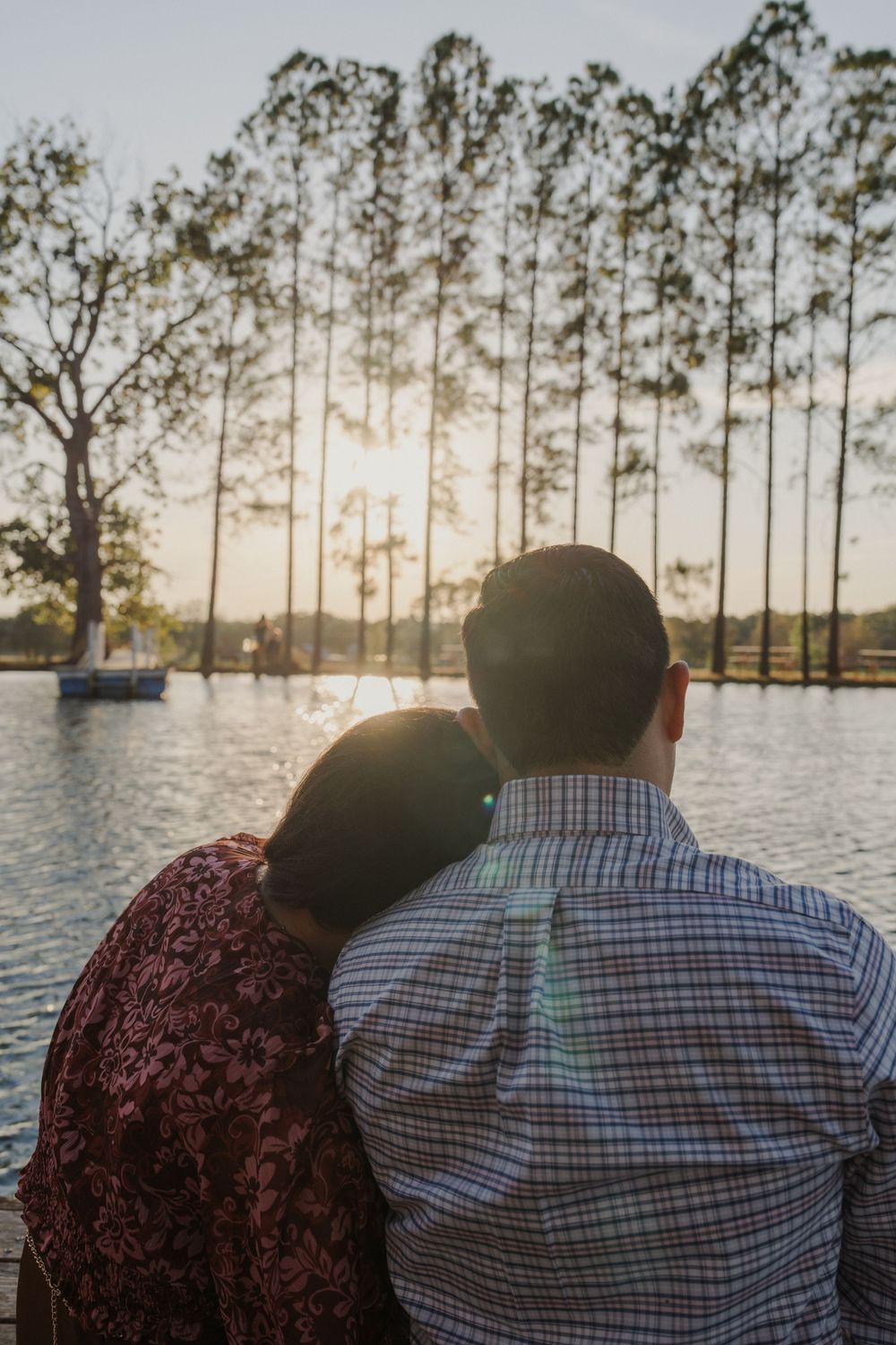 A couple sits together watching the sunset over a peaceful lake surrounded by pine trees.