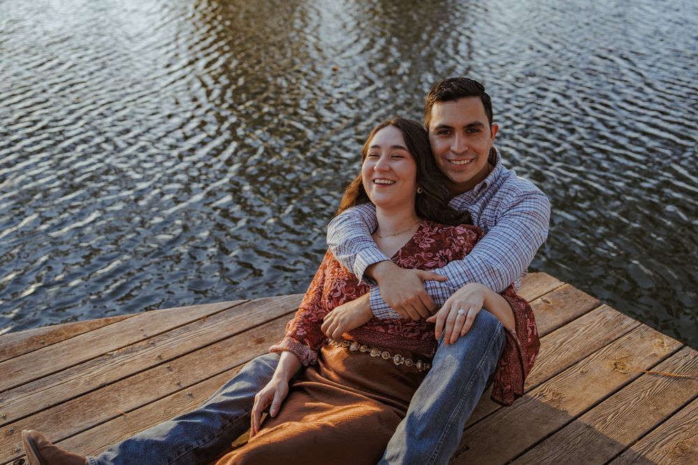 A couple shares a tender moment on a wooden dock overlooking a tranquil lake at sunset.