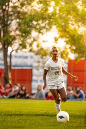 Soccer player in white uniform dribbling ball on green grass field at sunset.