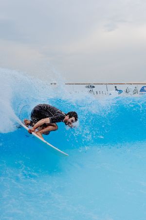 Surfer riding bright blue wave on artificial wave machine.