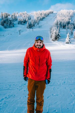 Snowboarder in red jacket and brown pants posing on snowy mountain slope.