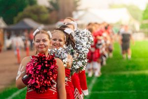 Cheerleaders with red and white pom poms performing at an outdoor sporting event.