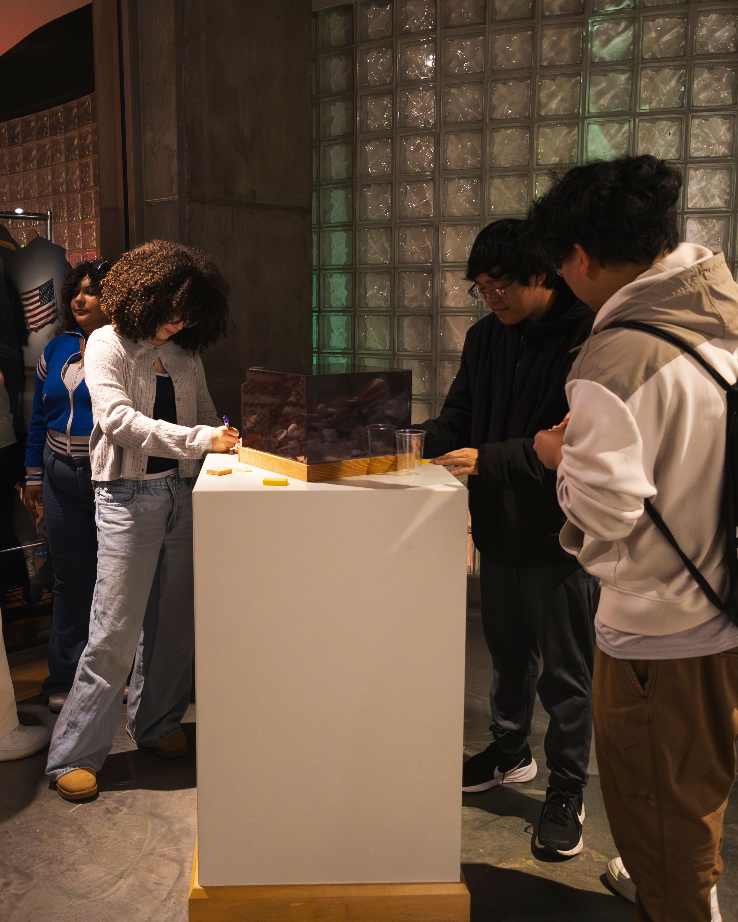 People gathered around white display boxes in an indoor exhibition space.