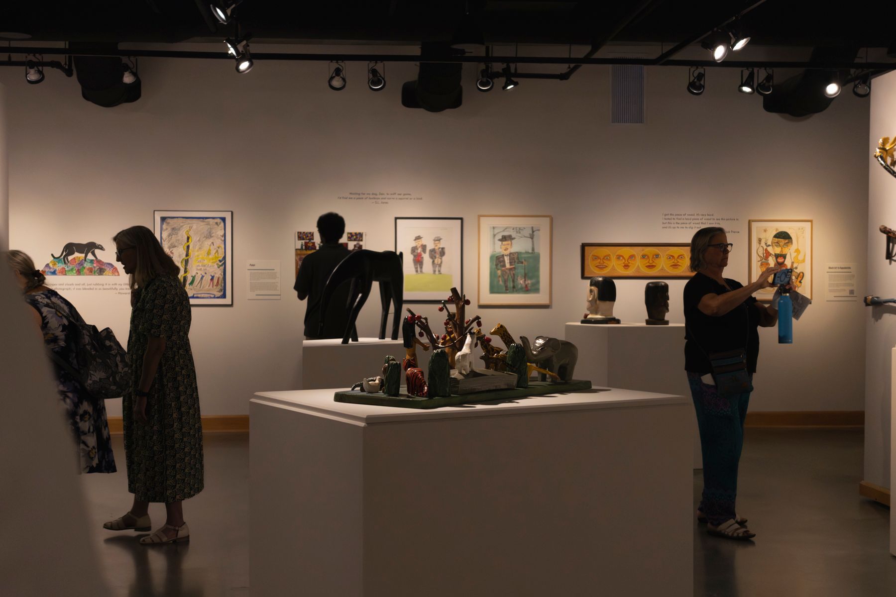Art gallery interior showing multiple exhibits and visitors in a well-lit space.