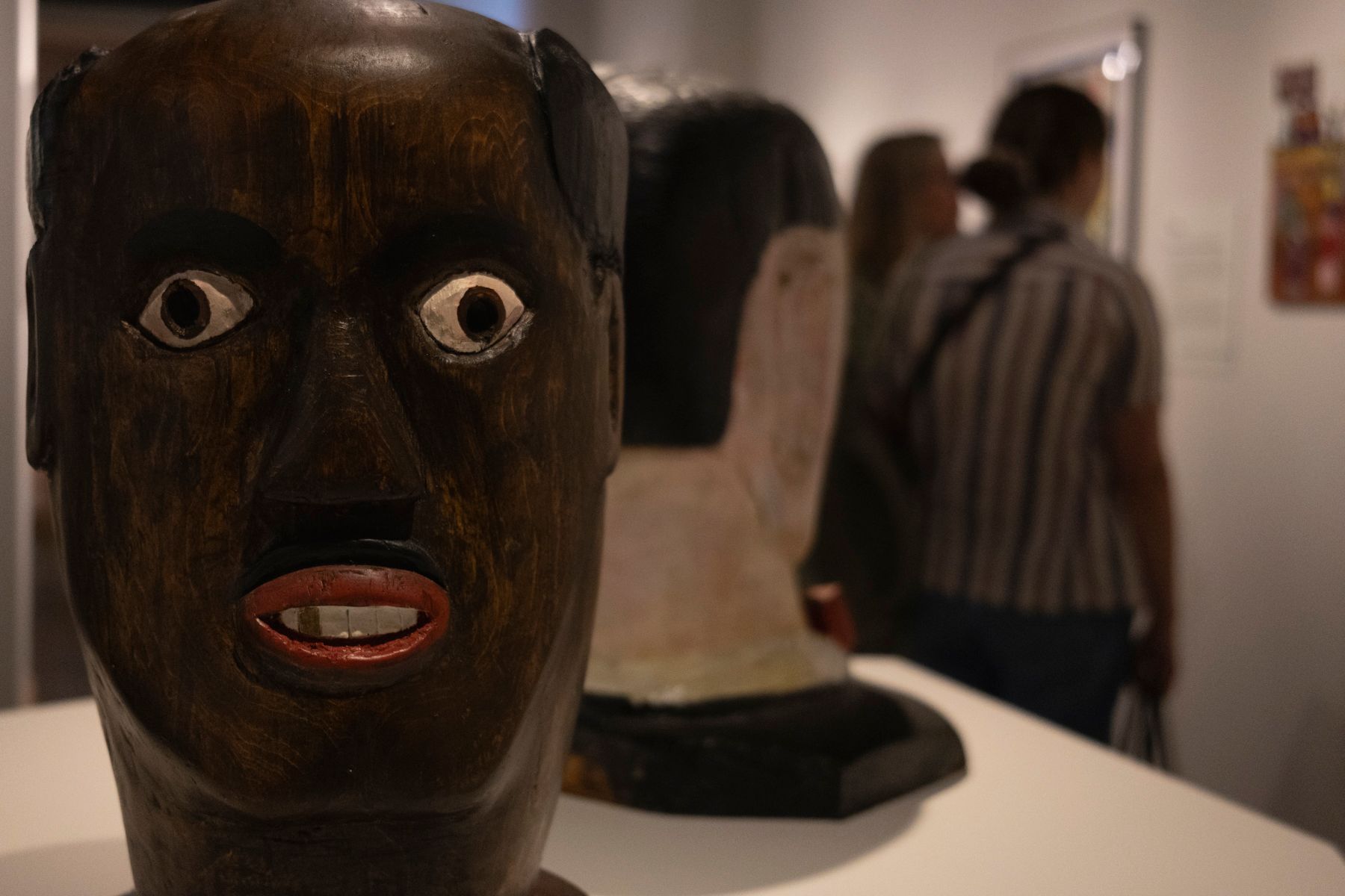Display of carved wooden masks with expressive faces in an art gallery setting.