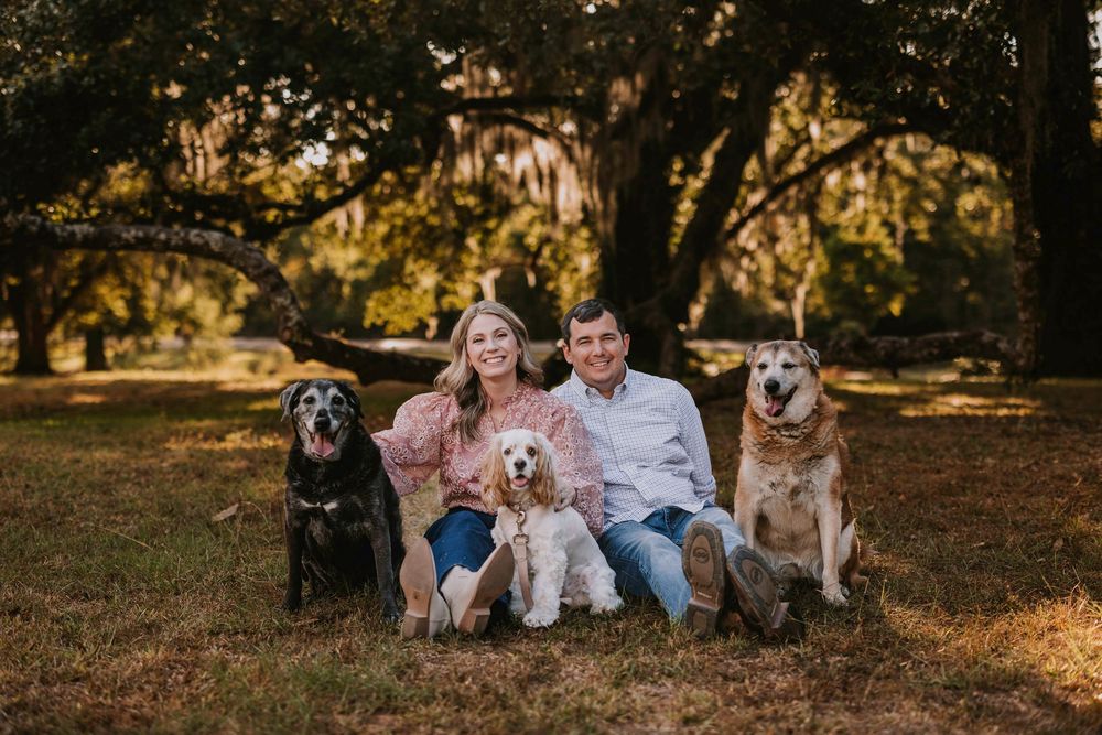 Family portrait with four dogs sitting together under trees in autumn setting.