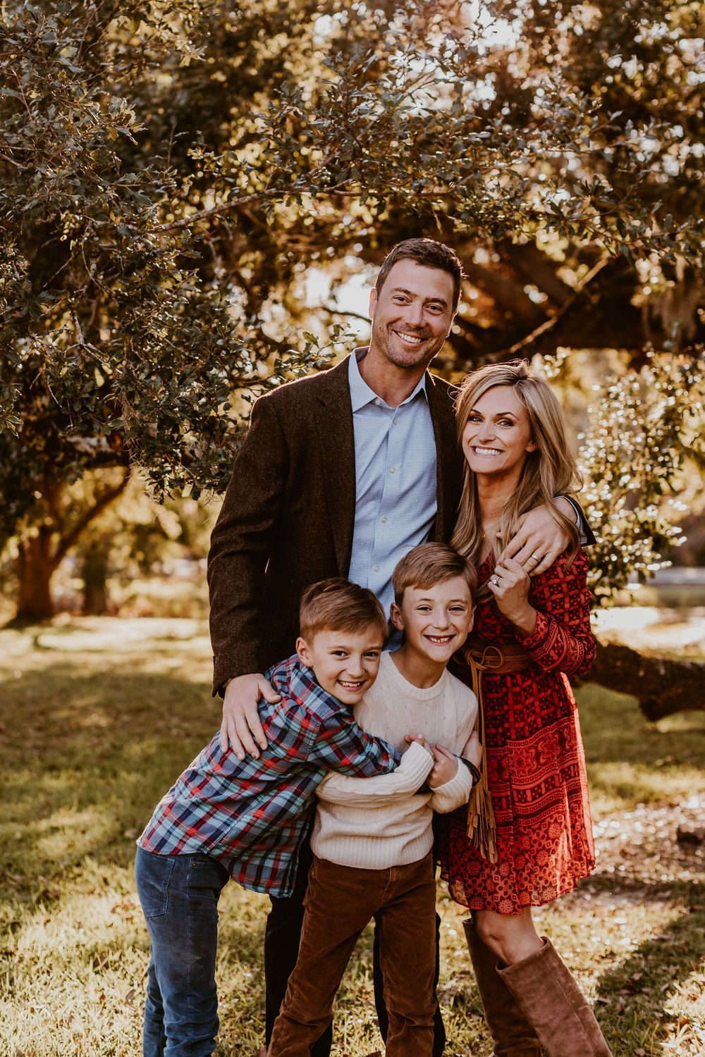 Family portrait taken outdoors with warm golden sunlight filtering through autumn trees.