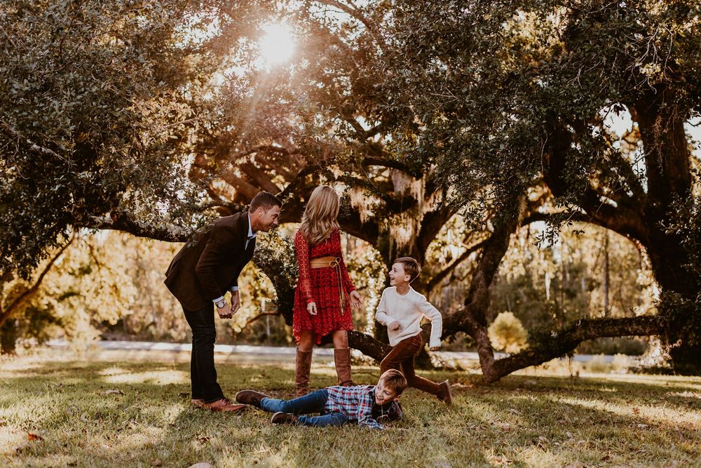 Playful family photo session in a park with golden sunlight and trees in the background.