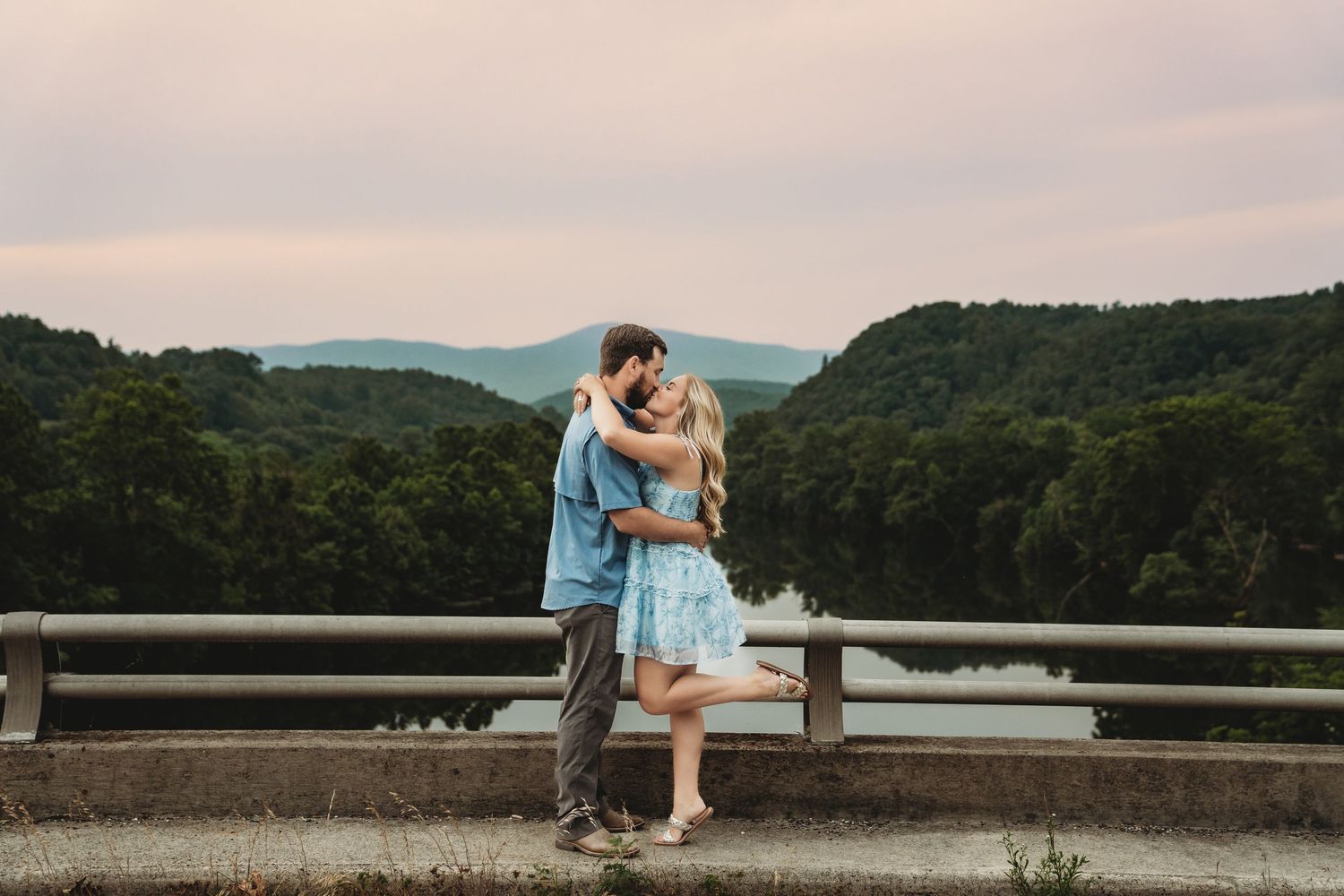 A couple shares tender moments on a lakeside overlook with mountain views.