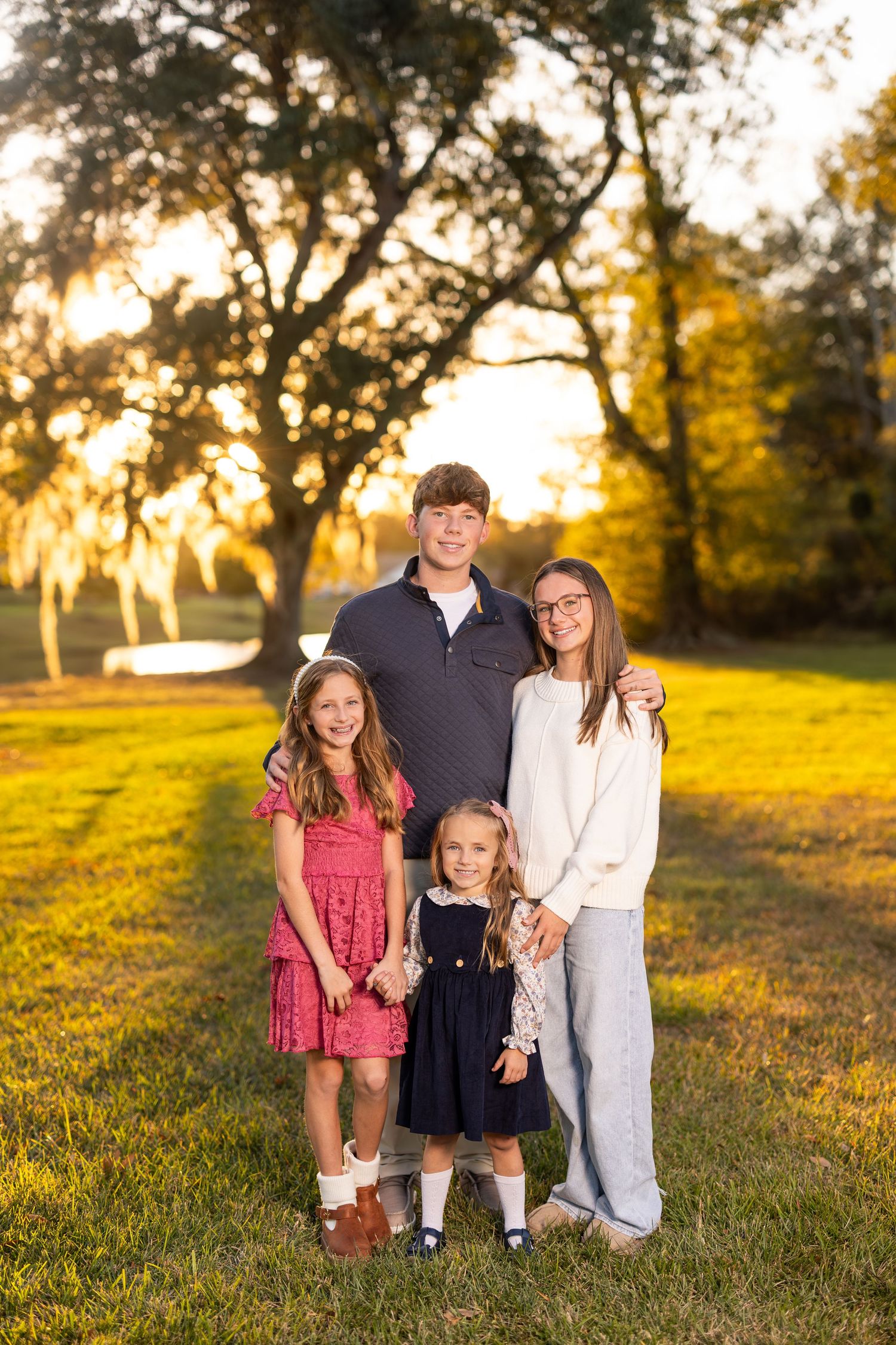 Family portrait at golden hour in grassy field with sunset lighting.