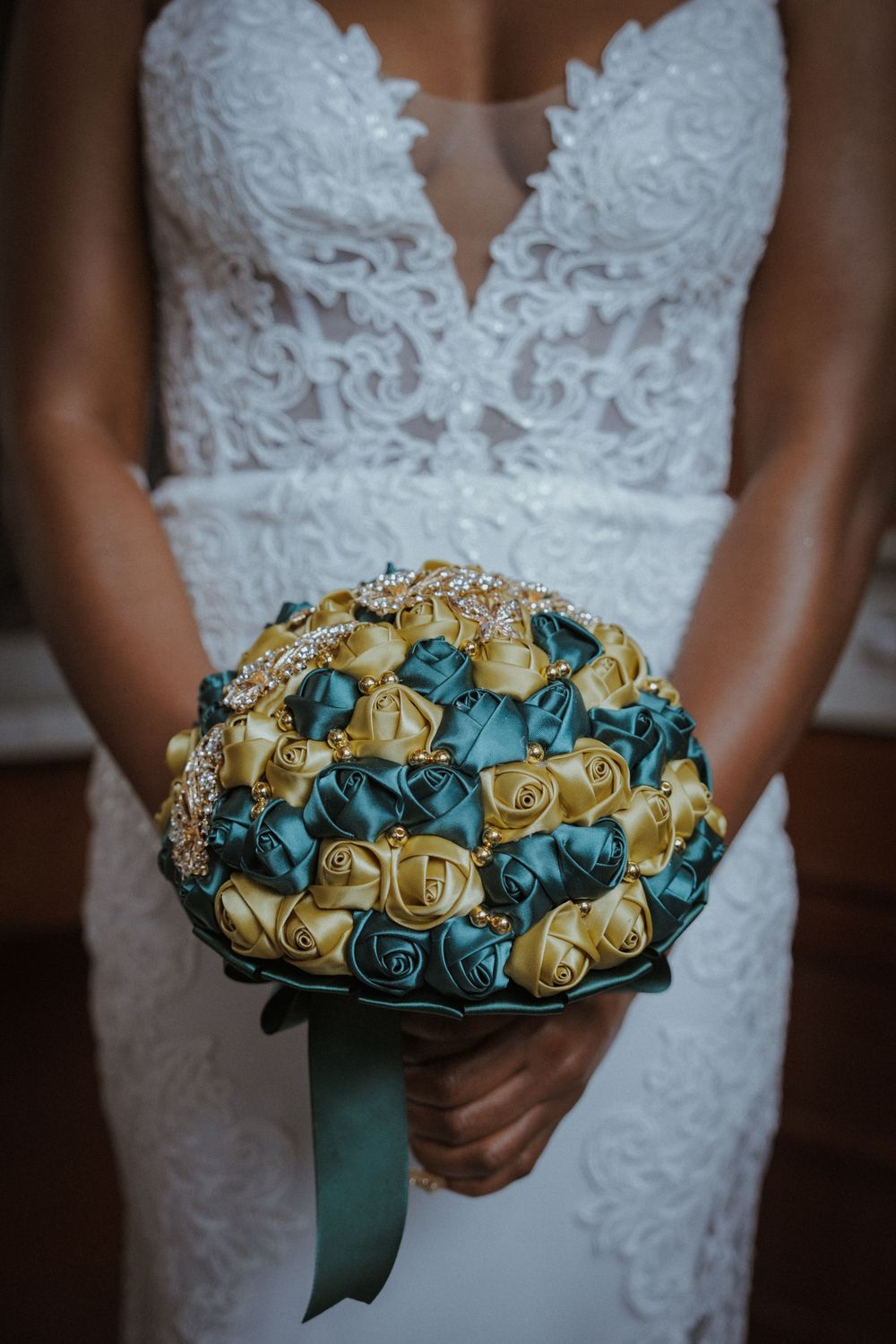 Wedding bouquet featuring teal and gold roses with ribbon wrap.