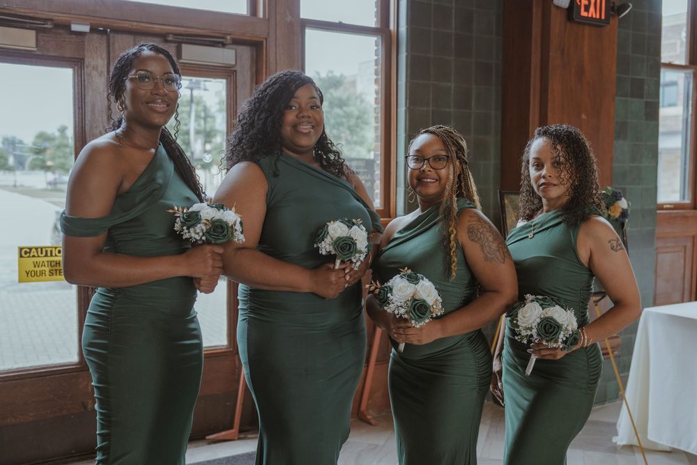 Bridesmaids in emerald green dresses holding white and teal bouquets.