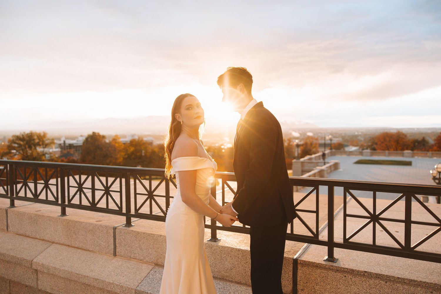 Bride and groom standing together on a balcony at the Utah State Capitol during golden hour