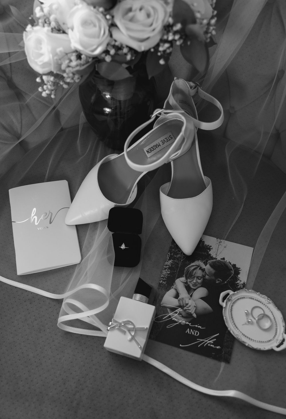 Black and white detail shot of elegant bridal shoes and roses arranged on the floor.