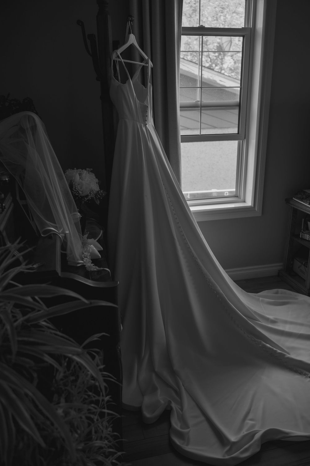 Wedding dress hanging by a window in dramatic black and white lighting.