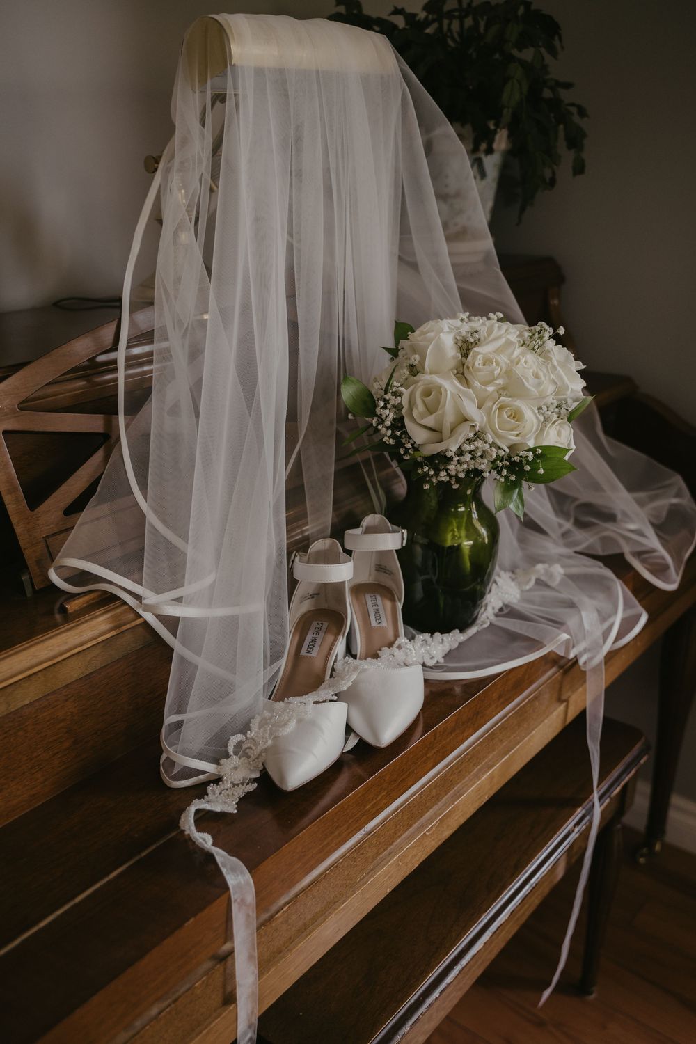 White bridal veil and shoes displayed with roses on wooden bench.