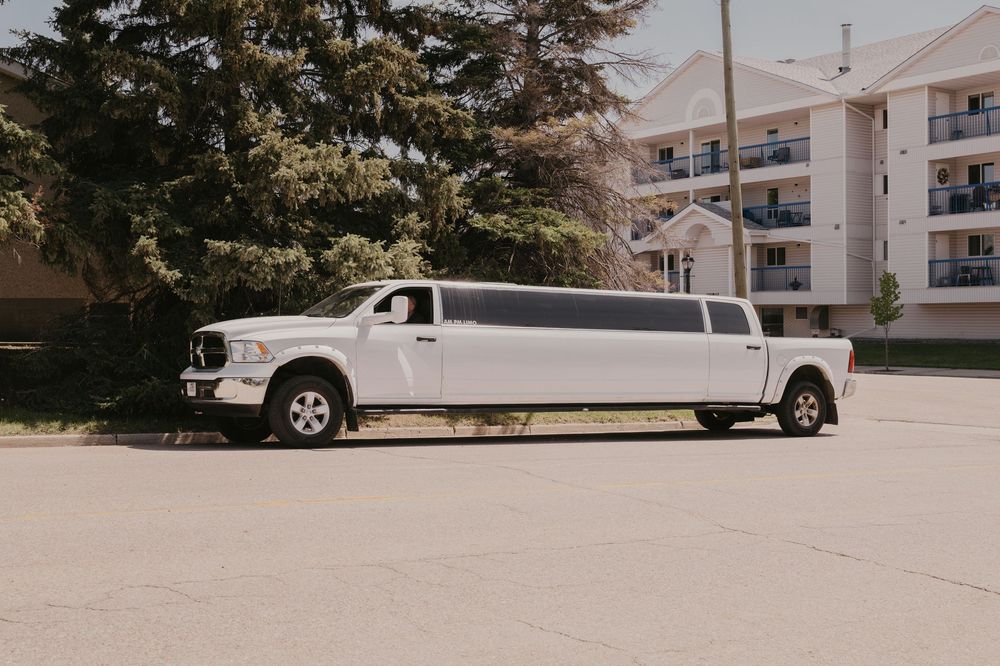 Row of white stretch limousines parked outside a modern apartment building on a sunny day.