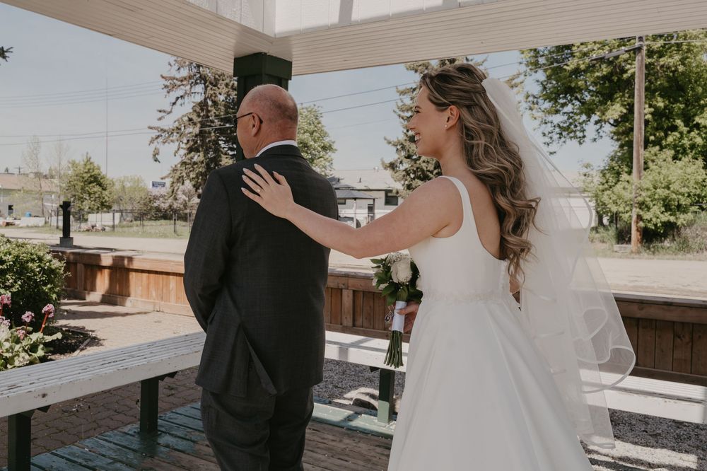 Wedding couple embracing outdoors with decorative greenery and architectural elements in the background.
