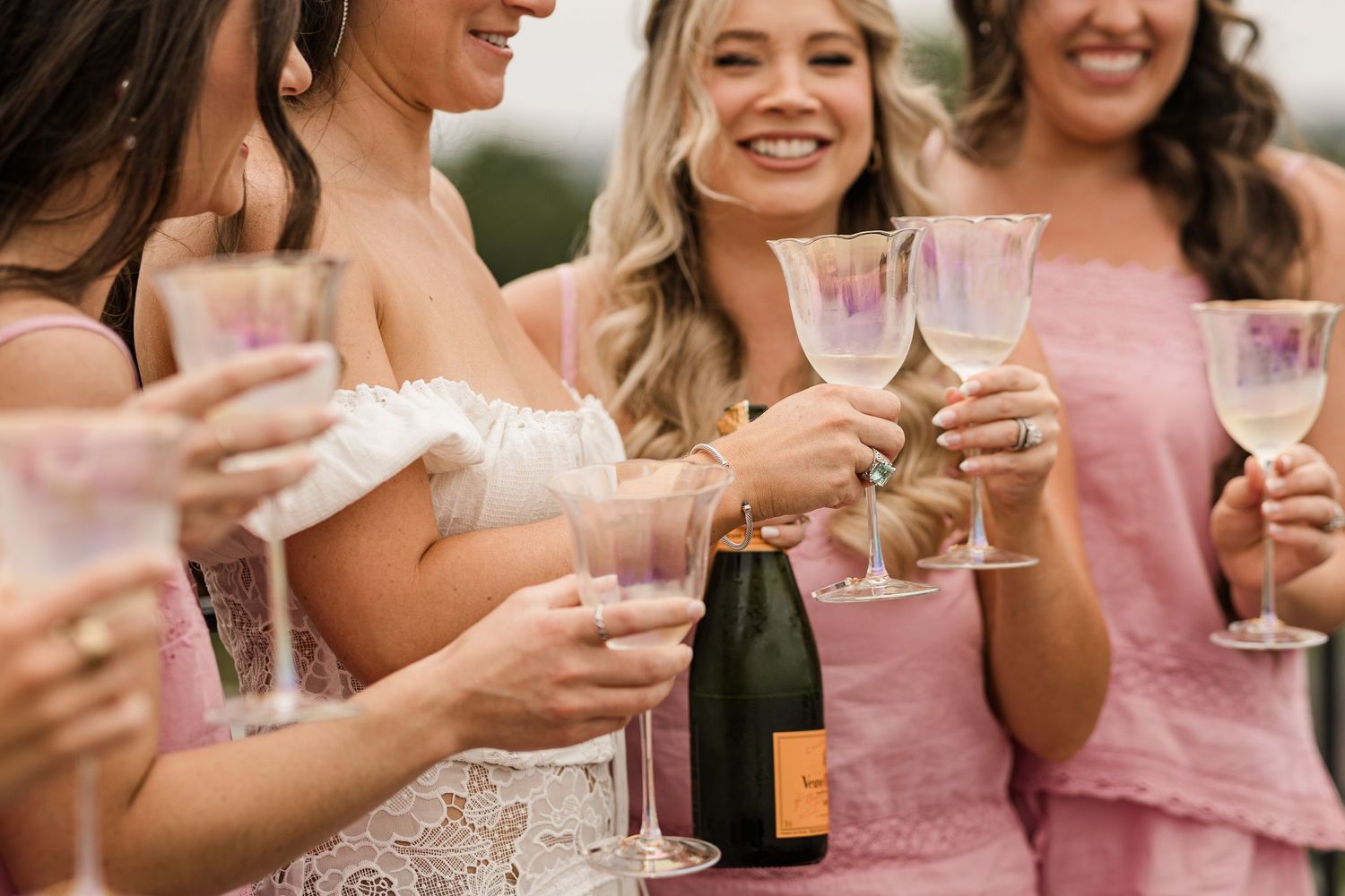 A group in pink dresses toasts with champagne glasses during an outdoor celebration.