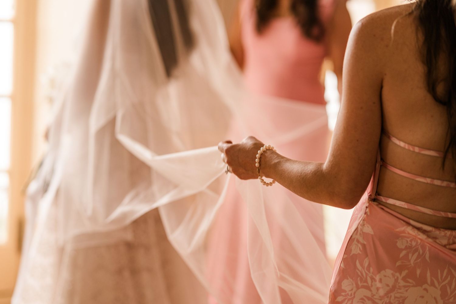 A row of elegant wedding dresses hanging on display with soft pink lighting illuminating their delicate details.