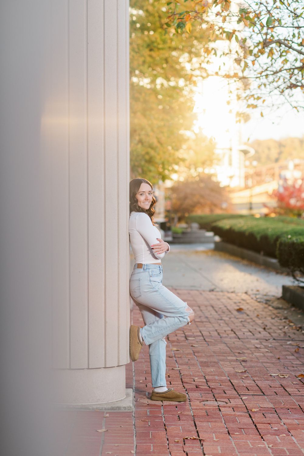 A person in casual attire leans against a white wall on a brick pathway during golden hour.