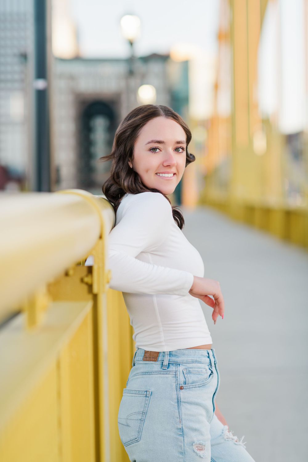 A casual portrait on a yellow bridge featuring a white long sleeve top and light denim jeans.