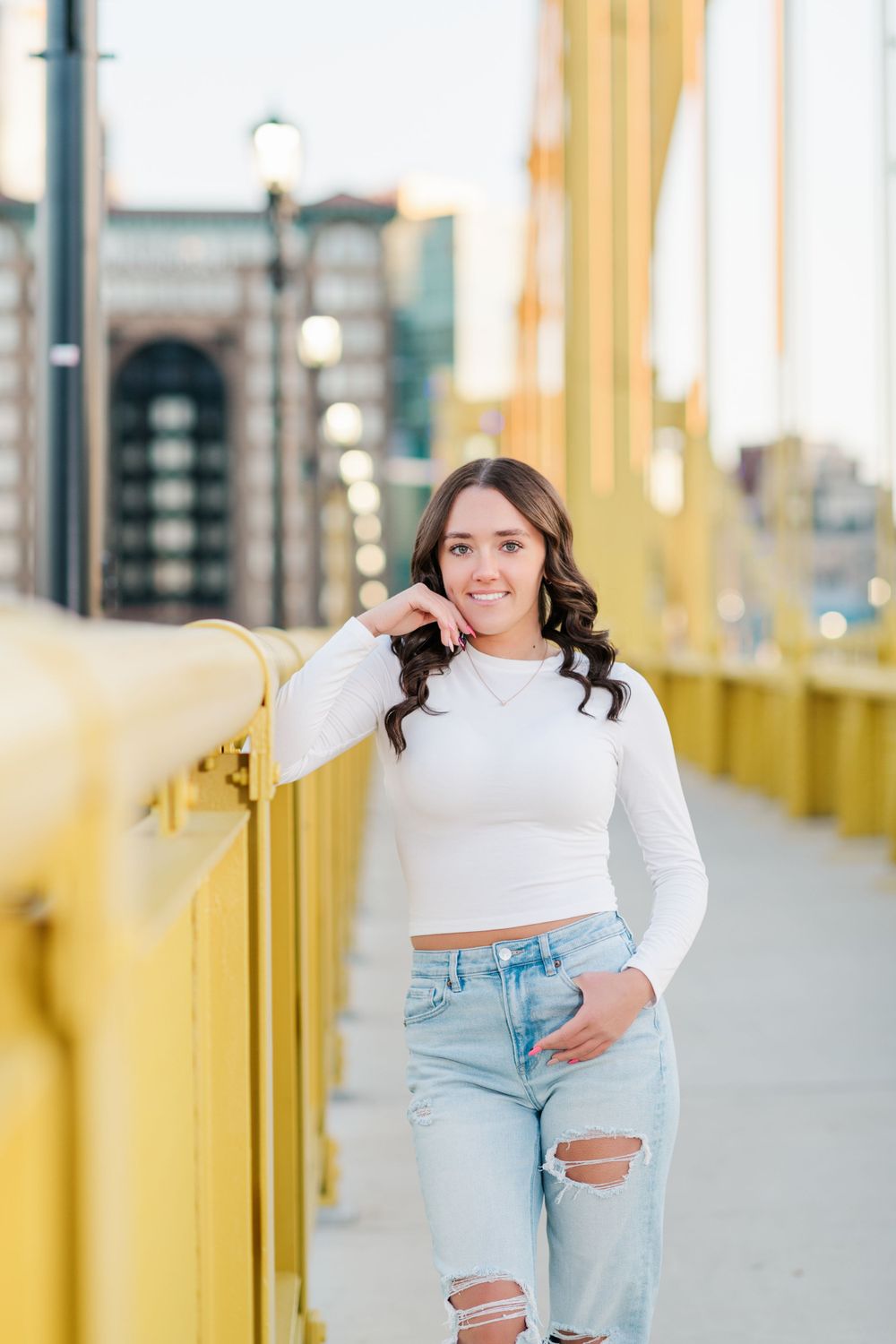 A person in a white crop top and ripped jeans poses on a yellow bridge during an outdoor photo session.