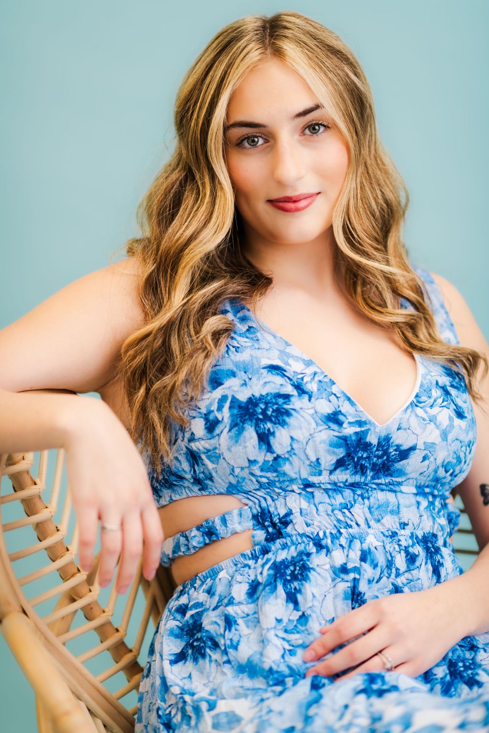 Someone wearing a blue and white floral dress poses in a wooden chair against a light blue background.
