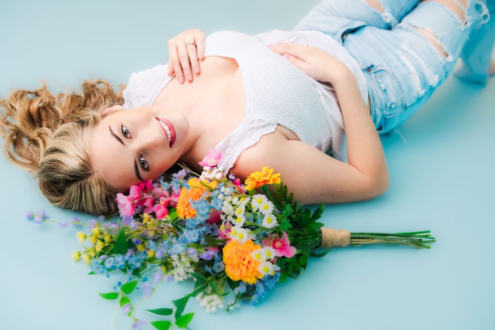 Laying on blue backdrop, someone rests beside vibrant spring bouquet with orange roses and wildflowers.