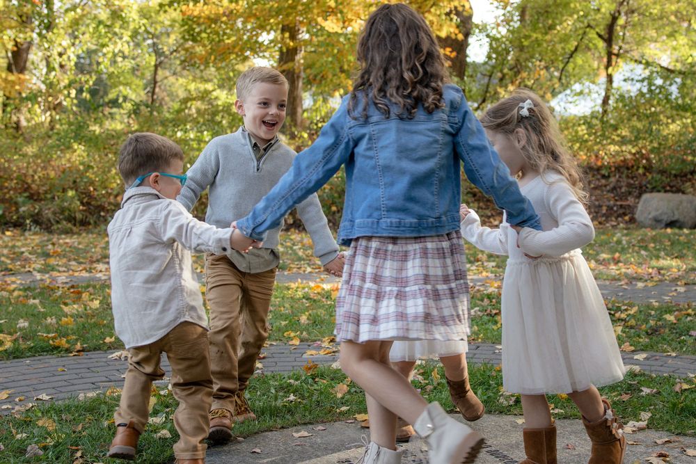 Children playing and dancing together in park during fall season.