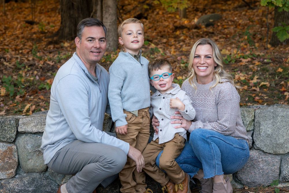Family of four sits together on stone wall during autumn photo session.