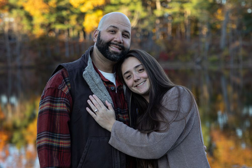 Couple in warm clothing embracing with autumn colors and lake reflection in background.