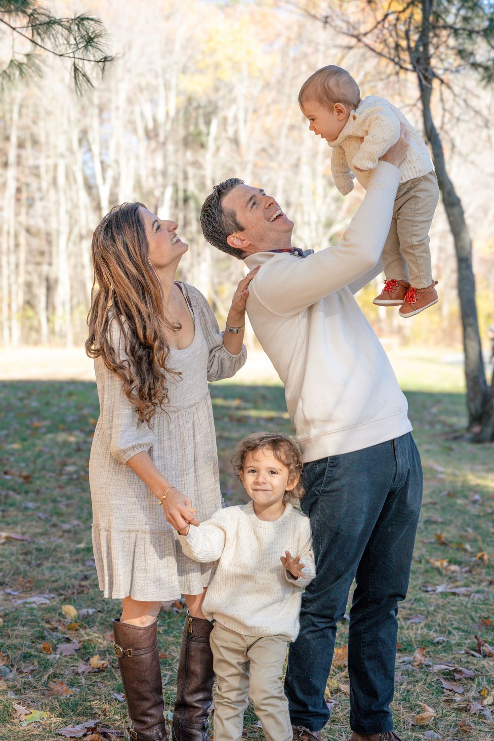 Family plays and laughs together during outdoor photo session in wooded setting.