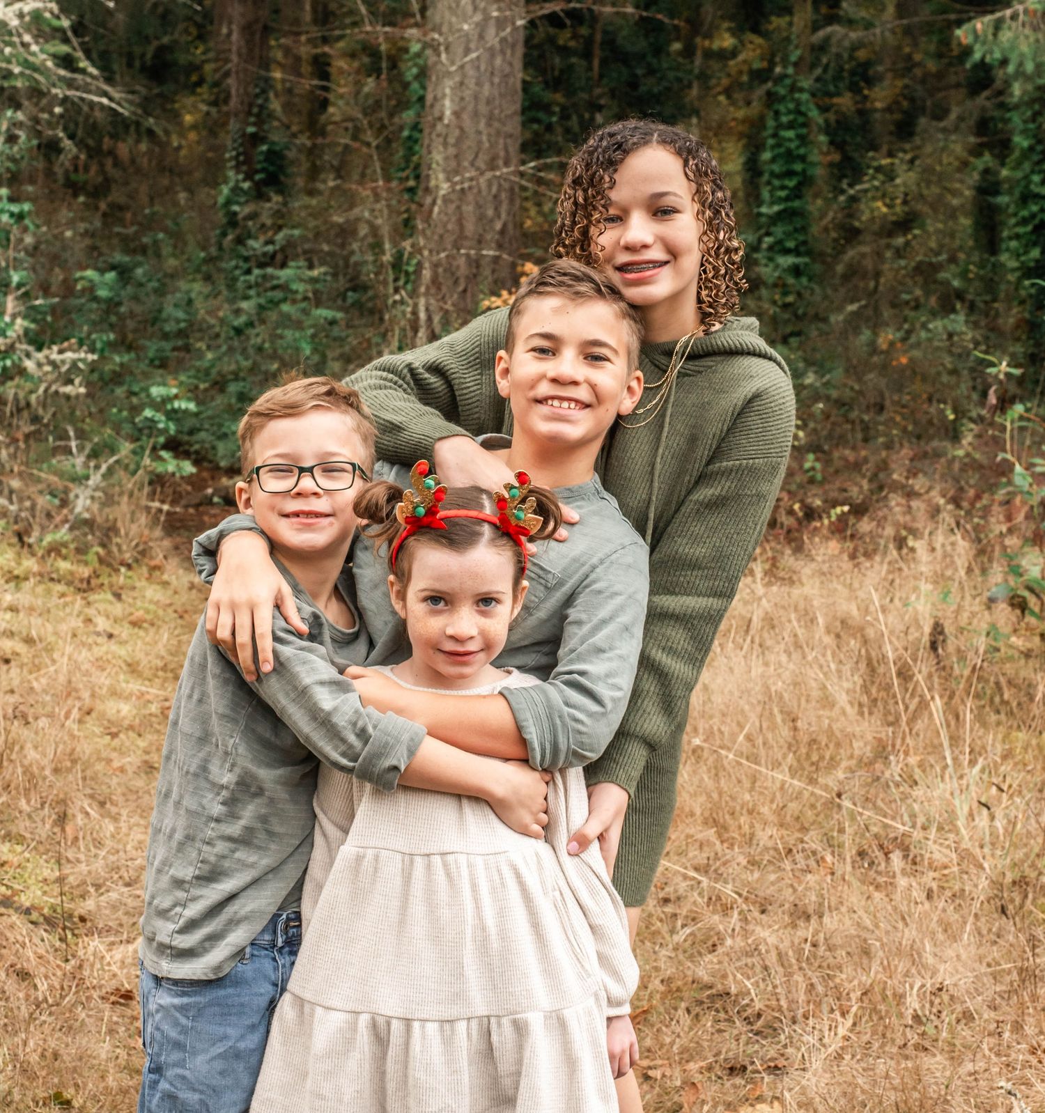 Two siblings share a warm embrace while standing in a grassy field with trees in the background.