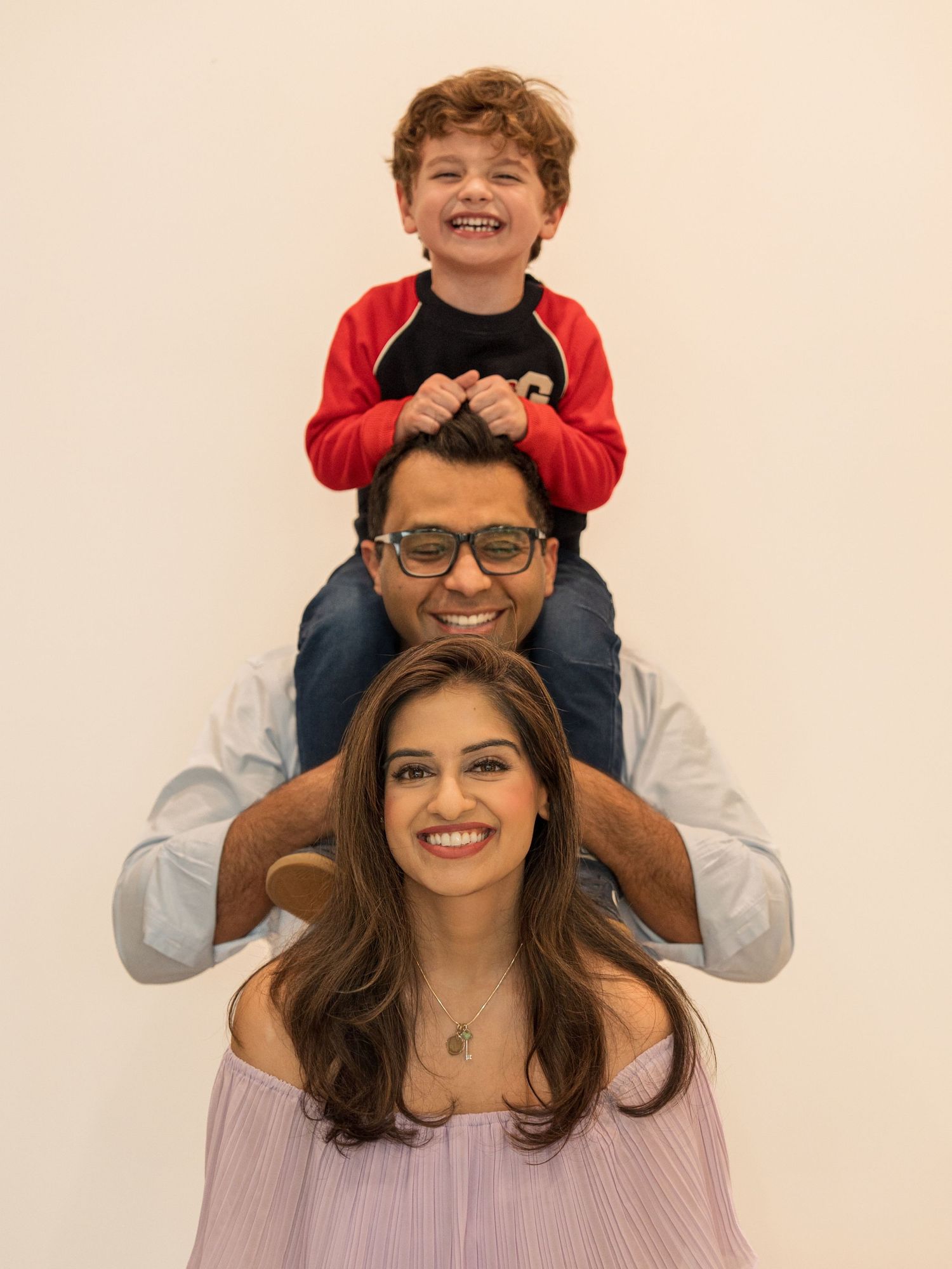 A joyful family portrait showing piggyback rides and smiles against a light colored background.