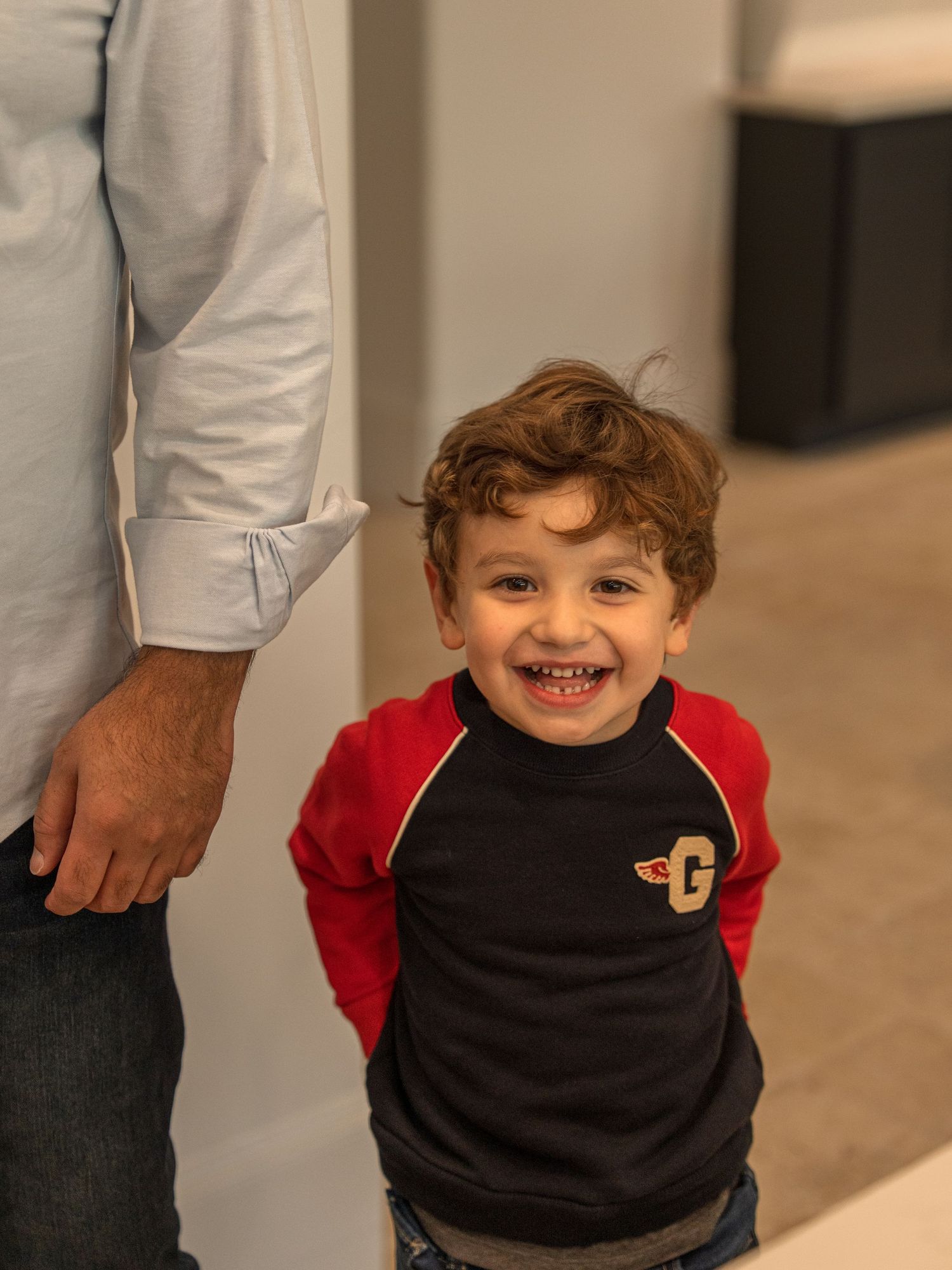 A toddler wearing a black and red Mickey Mouse shirt smiles while playing indoors.