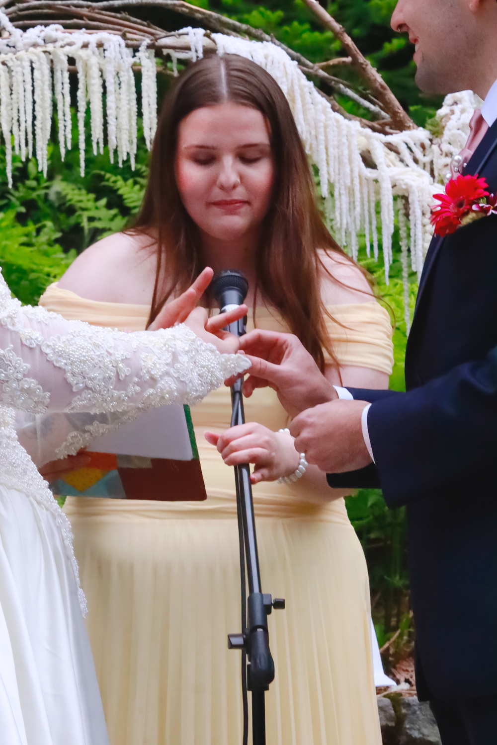 Wedding ceremony takes place under icicle decorations with speakers and guests in pastel attire.