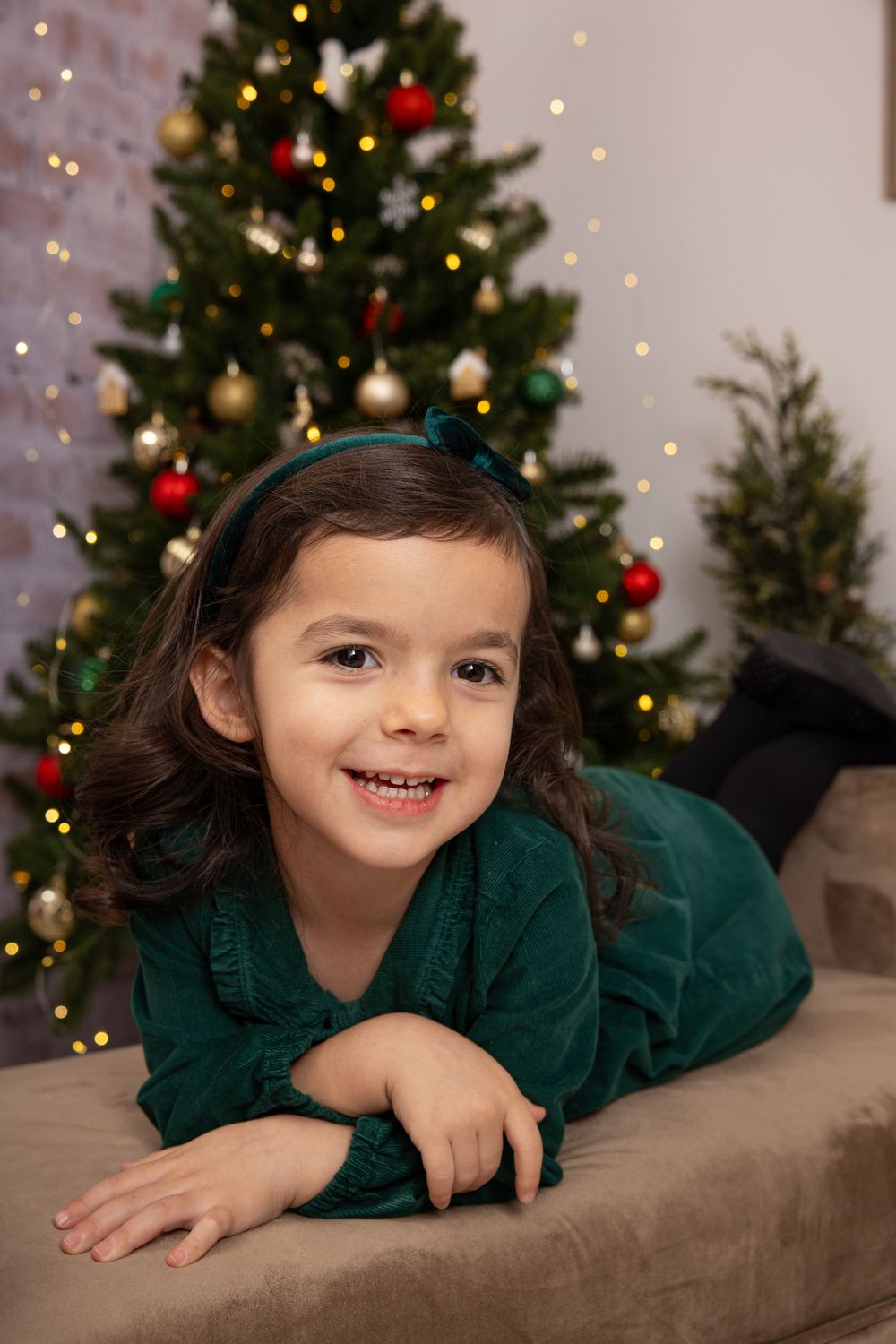 Holiday portrait setup featuring emerald green outfit against decorated Christmas tree background.