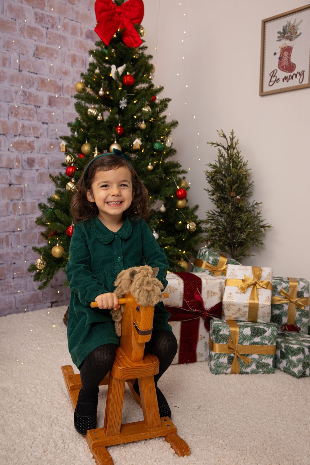A cozy holiday setting with a green-dressed figure on a wooden rocking horse near a Christmas tree.
