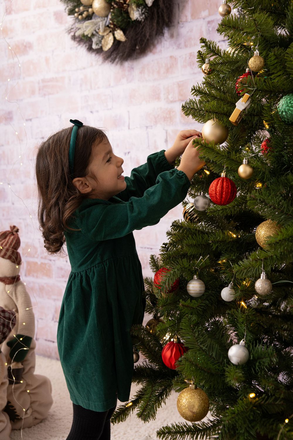 Someone in a green dress decorating a Christmas tree with gold and red ornaments.