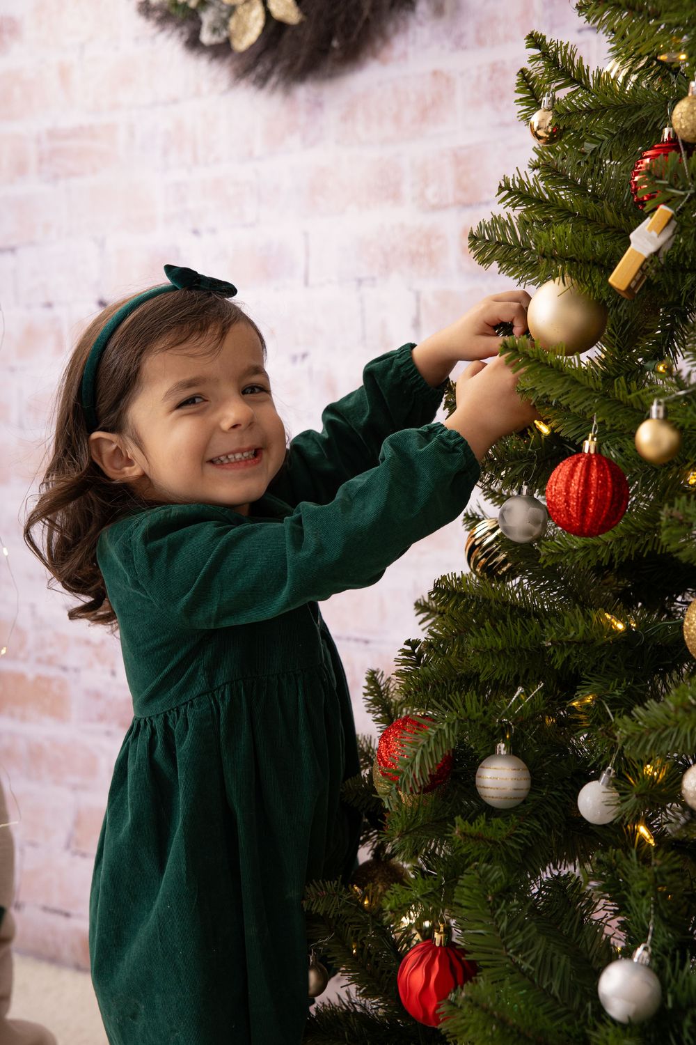 Someone reaching up to decorate a Christmas tree with ornaments while wearing a green dress.