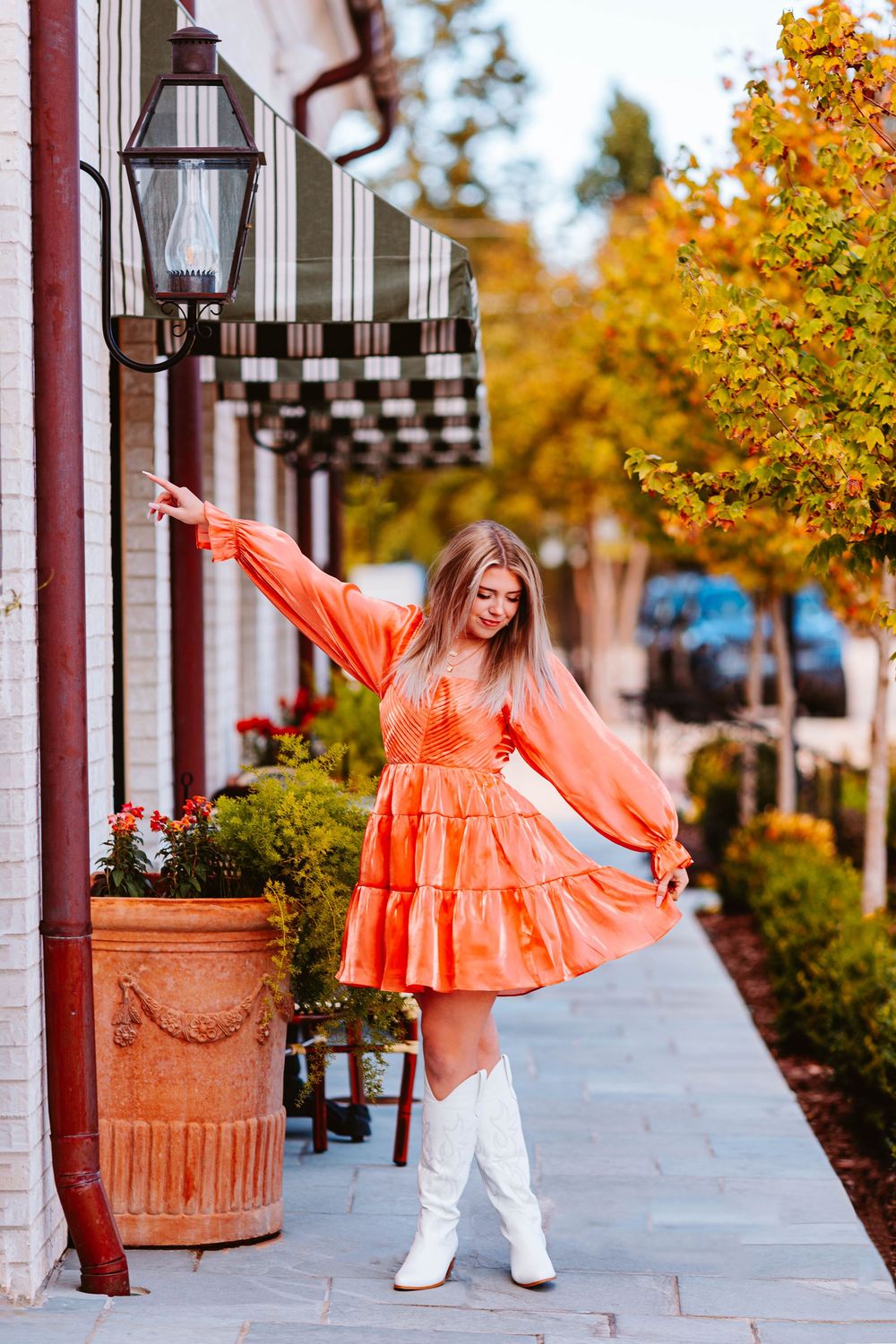 Person in flowing coral dress twirls on sidewalk near decorative planters.