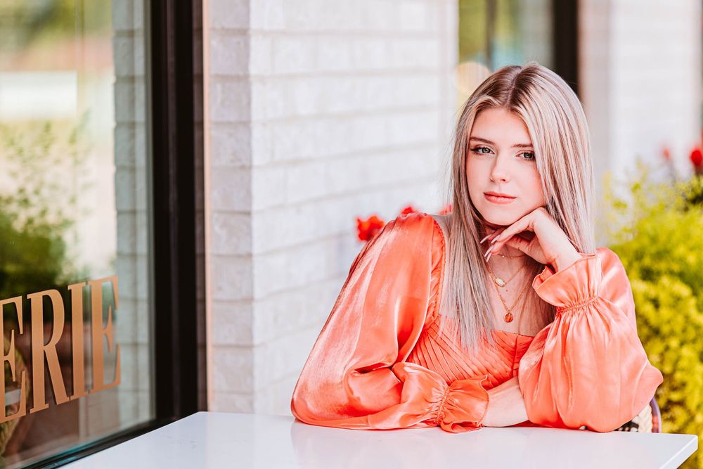 Multiple poses of a person in a coral dress against a white brick wall and cafe setting.