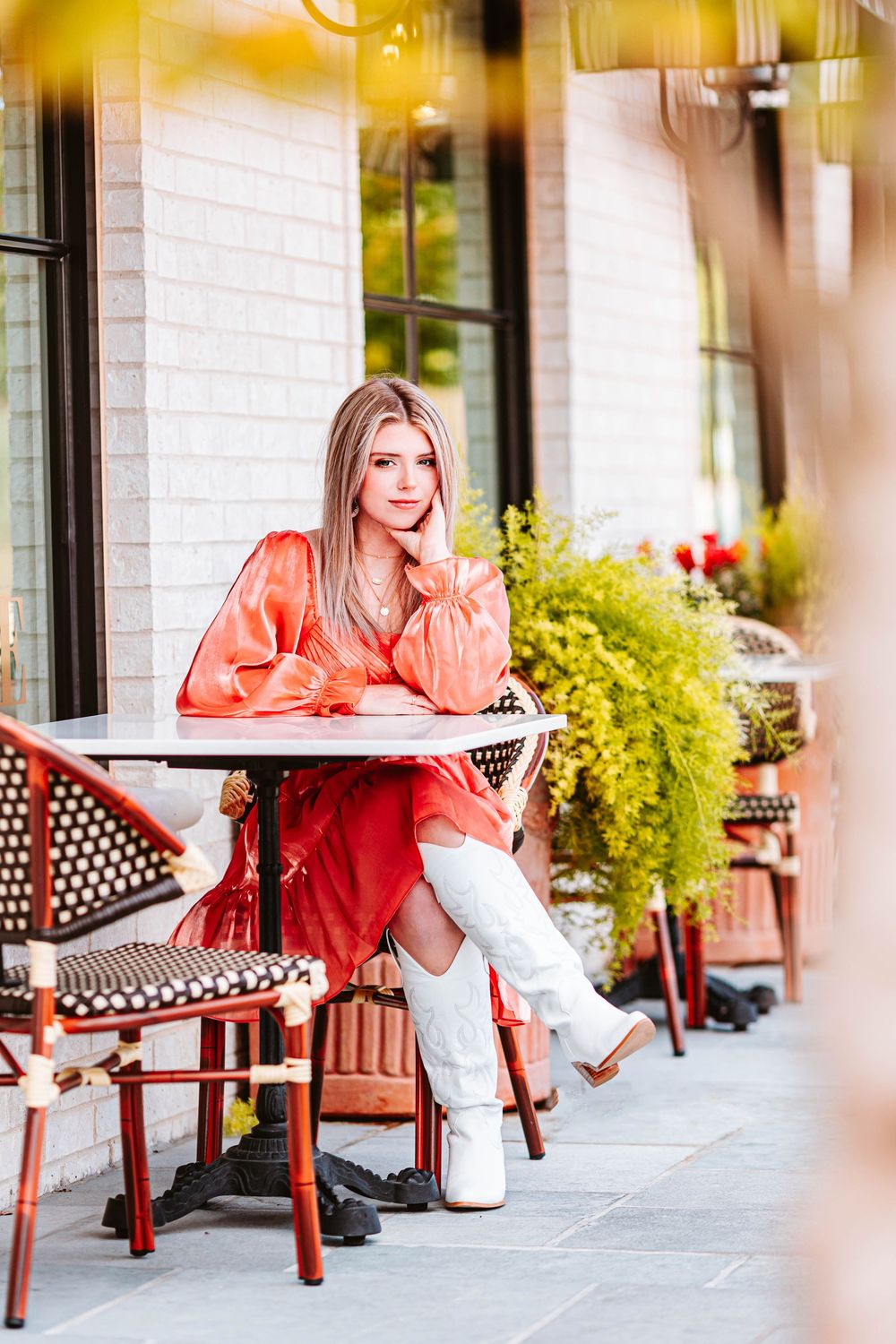 Fashion editorial series at a cafe patio with someone modeling a coral dress and white boots.