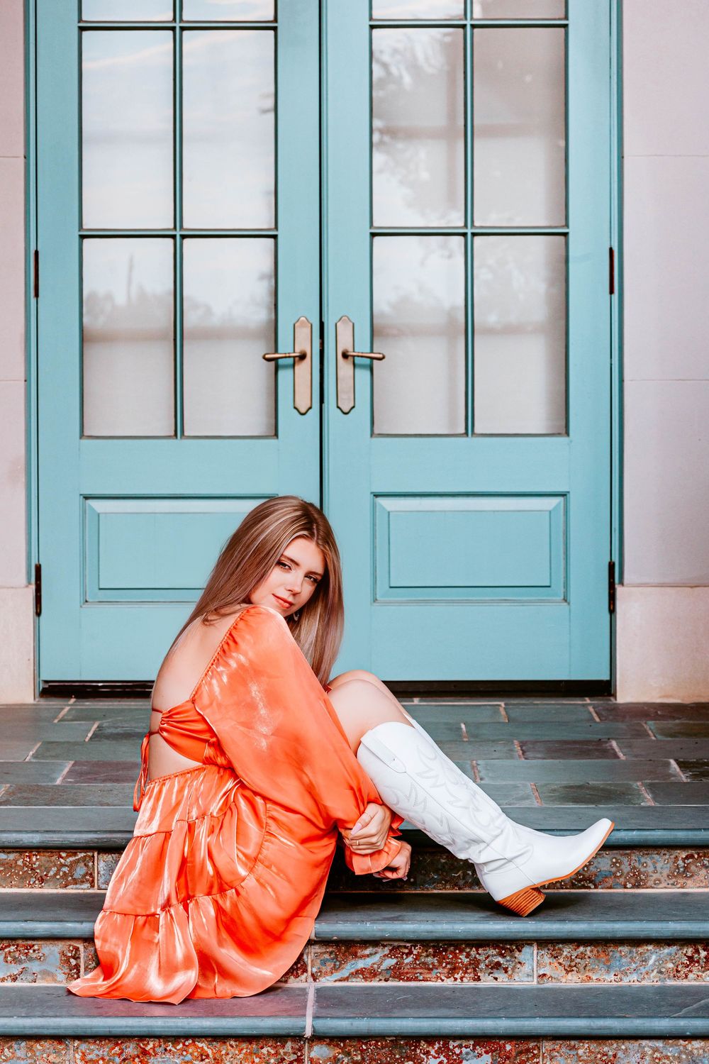 Artistic photo series of someone in an orange dress posing by turquoise doors.