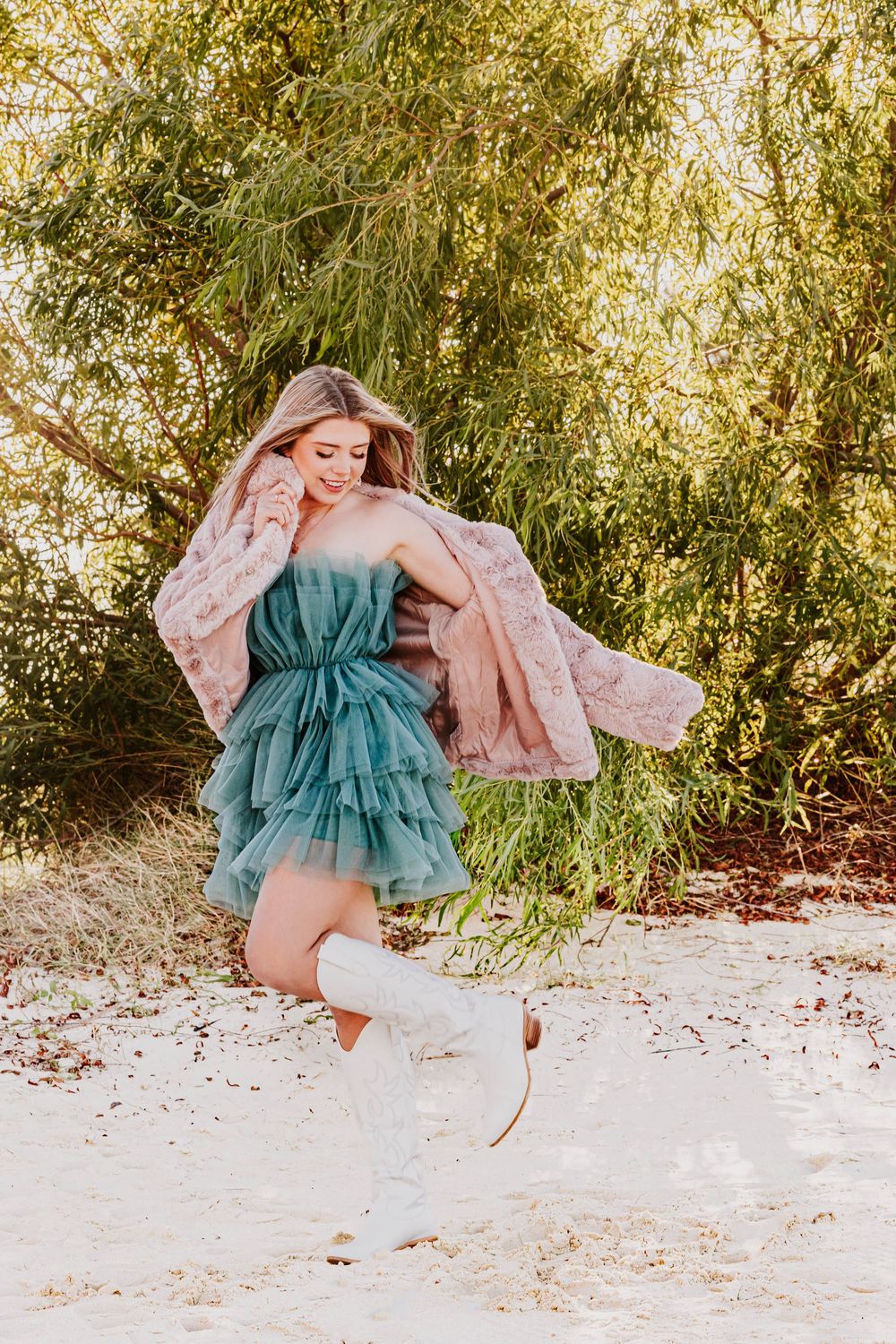 Dynamic poses in a pink fur jacket and teal tulle dress on snowy ground.