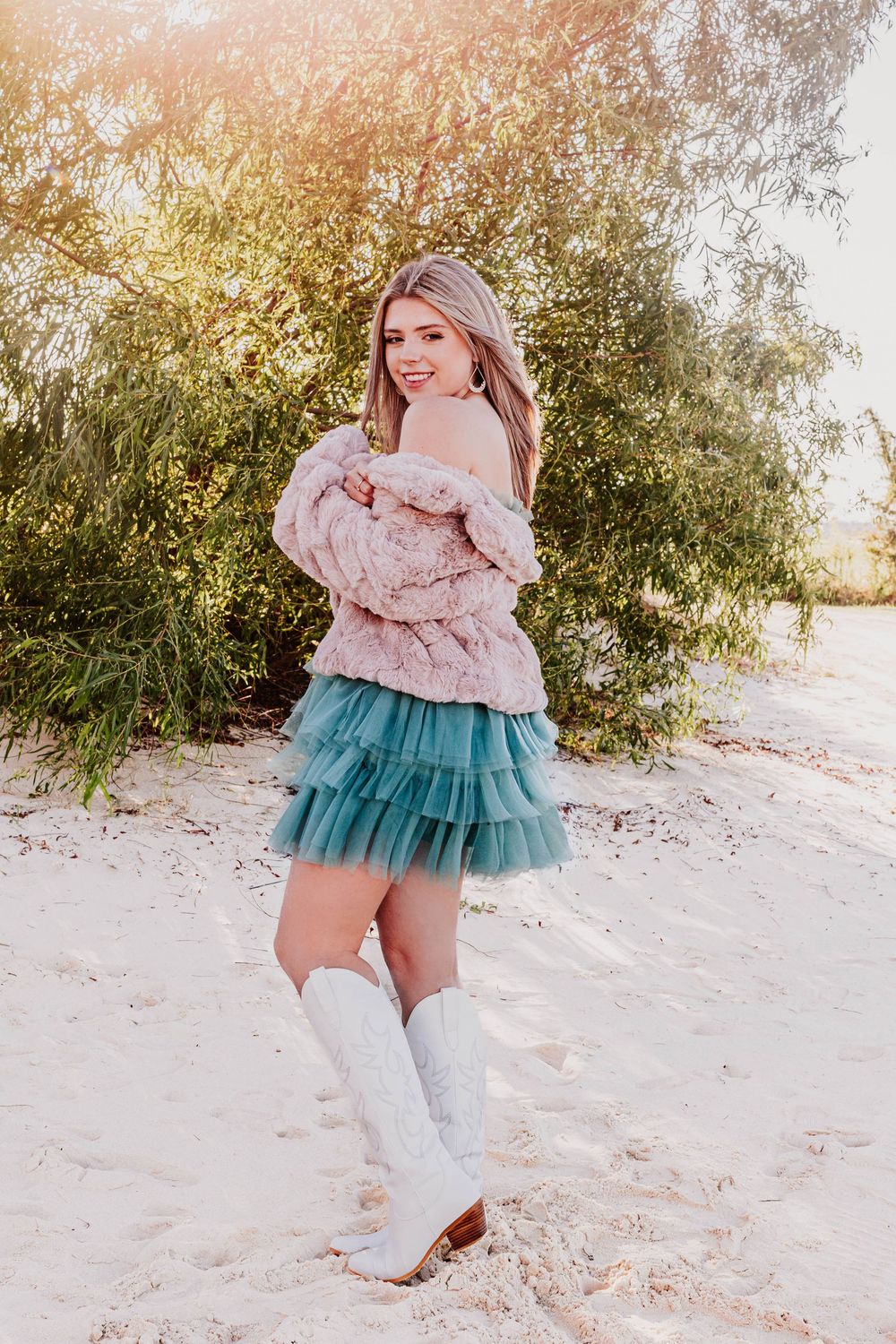Fashion photos of someone wearing white boots and a teal tulle dress in a snowy setting.